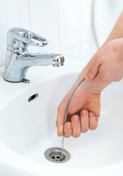 Person cleaning bathroom sink drain with flexible metal snake tool