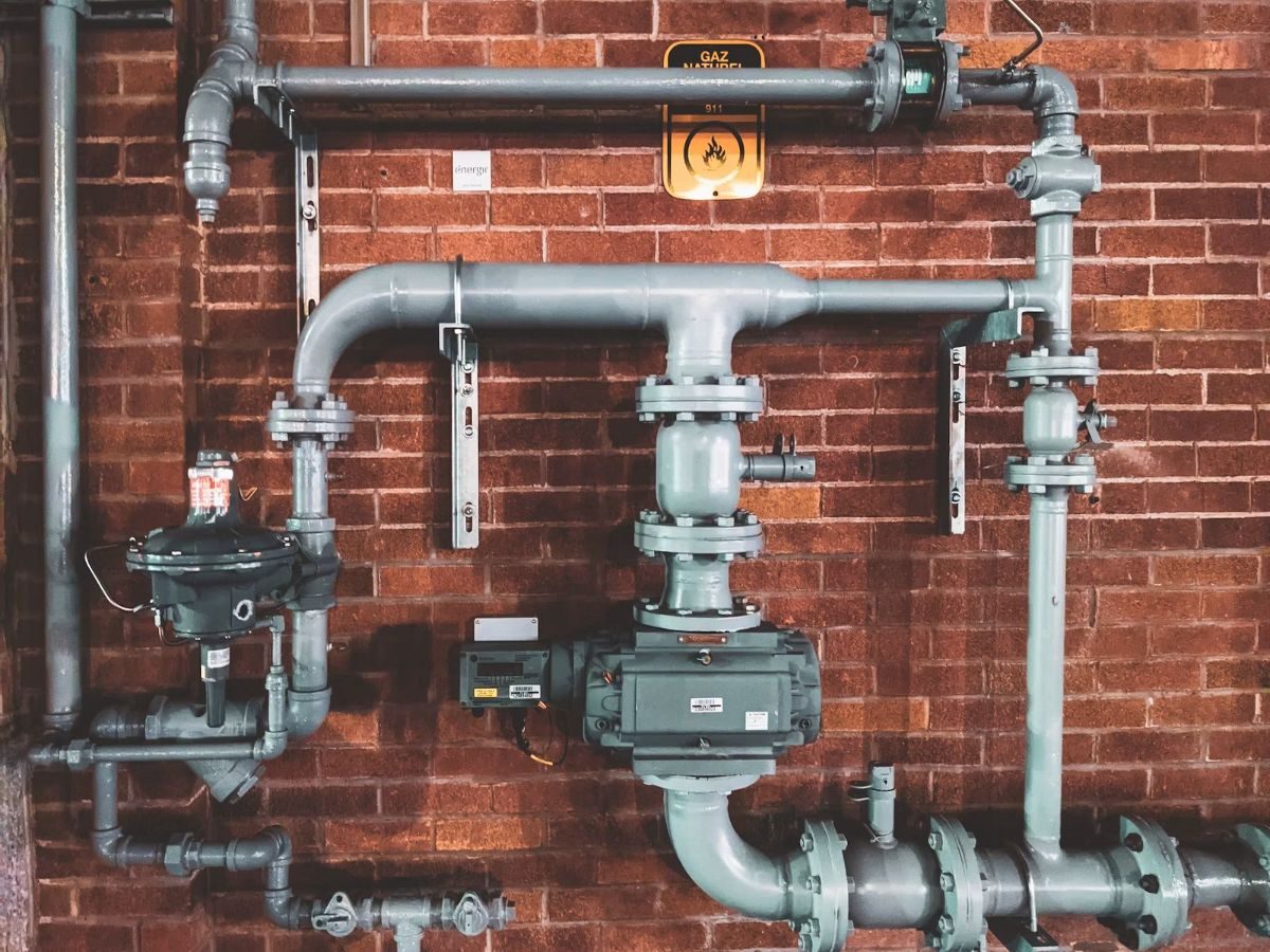 External gas pipes and regulators mounted on red brick wall with safety signage