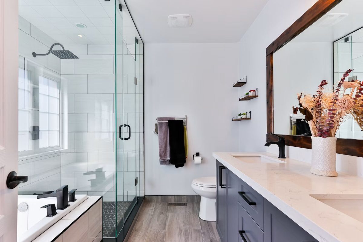 Modern bathroom with white subway tiles, glass shower enclosure, dark wood-framed mirror, and dual vanity sink