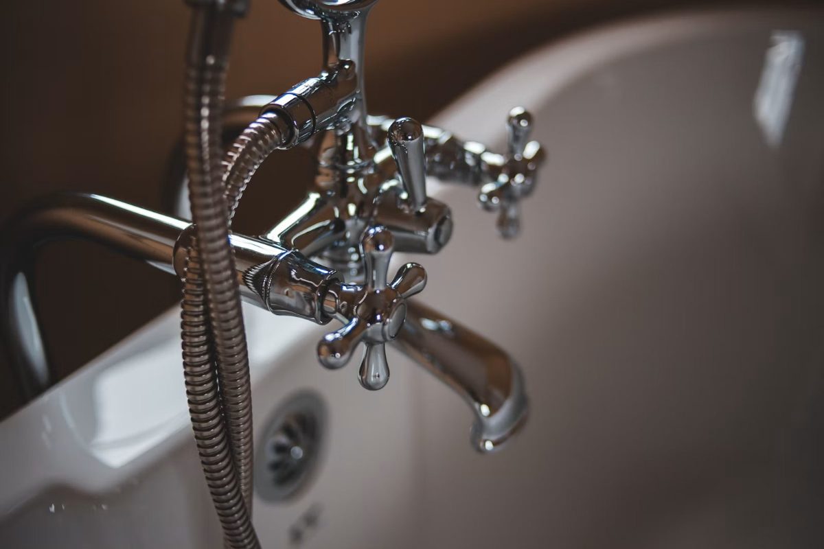 Chrome bathroom faucet with cross handles and flexible hose over white sink