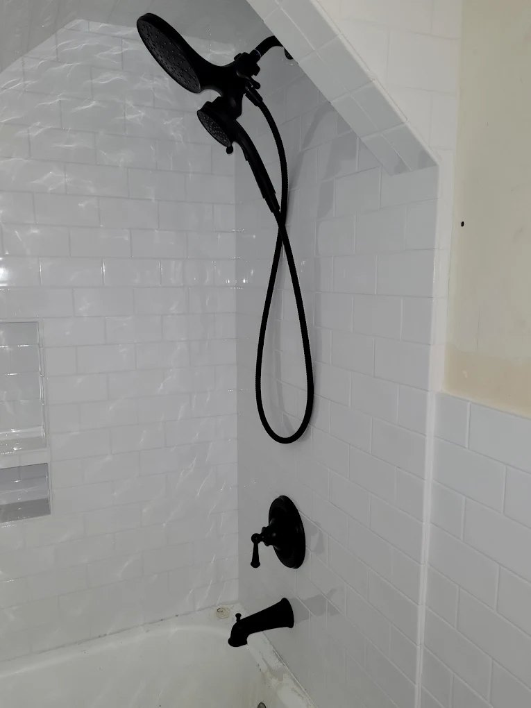 Black shower fixtures and handheld showerhead mounted on white subway tile bathroom wall