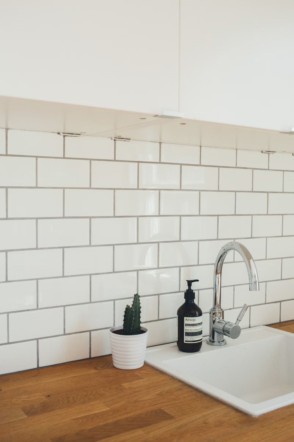 Modern kitchen sink with white subway tile backsplash, chrome faucet, and countertop decor
