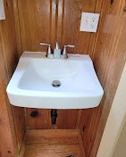 White pedestal sink with chrome faucet in wood-paneled bathroom