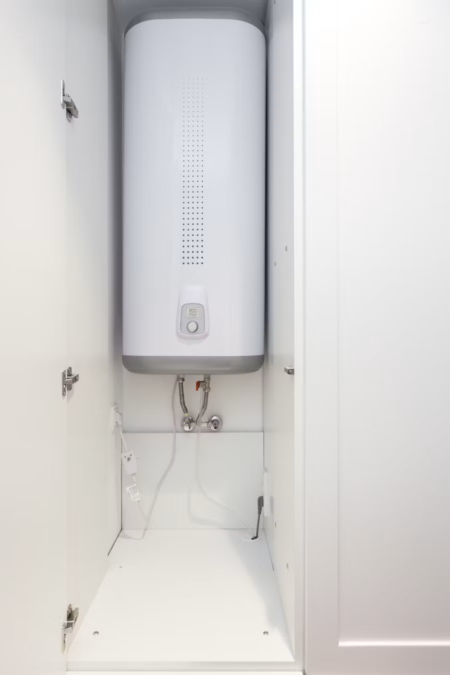 White electric water heater installed in wall cabinet with supply pipes and control panel